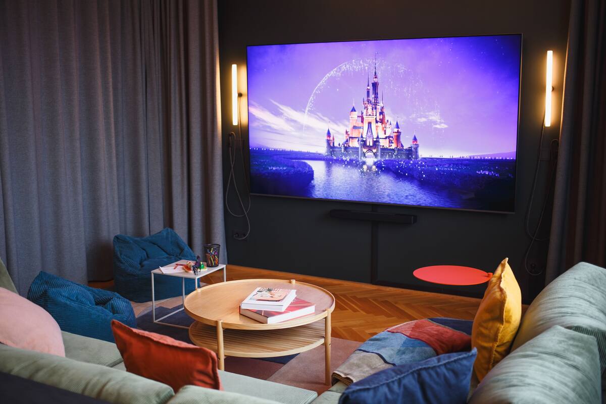 Ein modernes Wohnzimmer mit einem Flachbildfernseher, der eine Schlossansicht zeigt, einer Couch, einem Couchtisch und einem kleinen Beistelltisch mit Büchern.