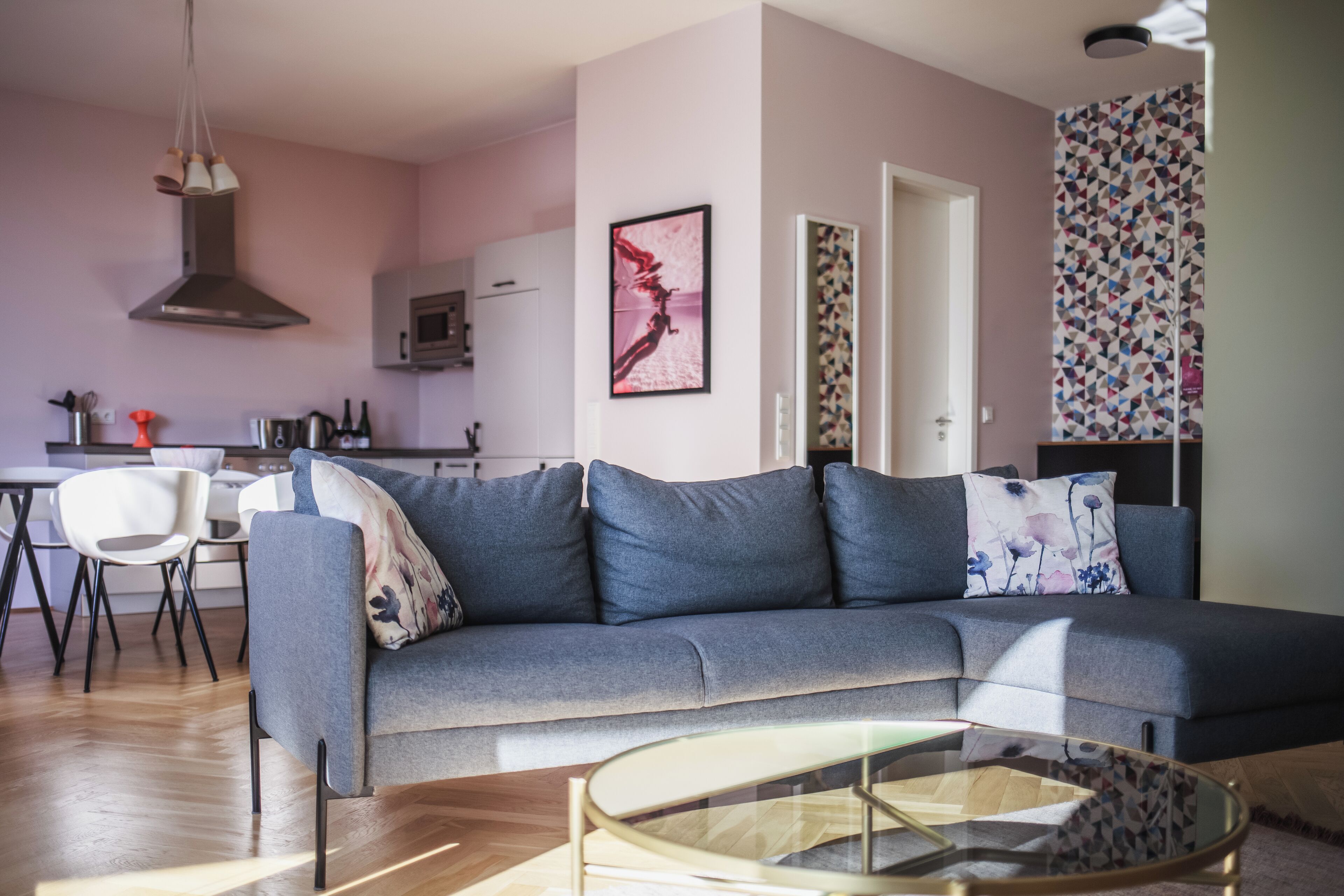 Una sala de estar moderna con un sofá gris, una mesa de centro de vidrio y una zona de comedor con una silla y una mesa blancos.