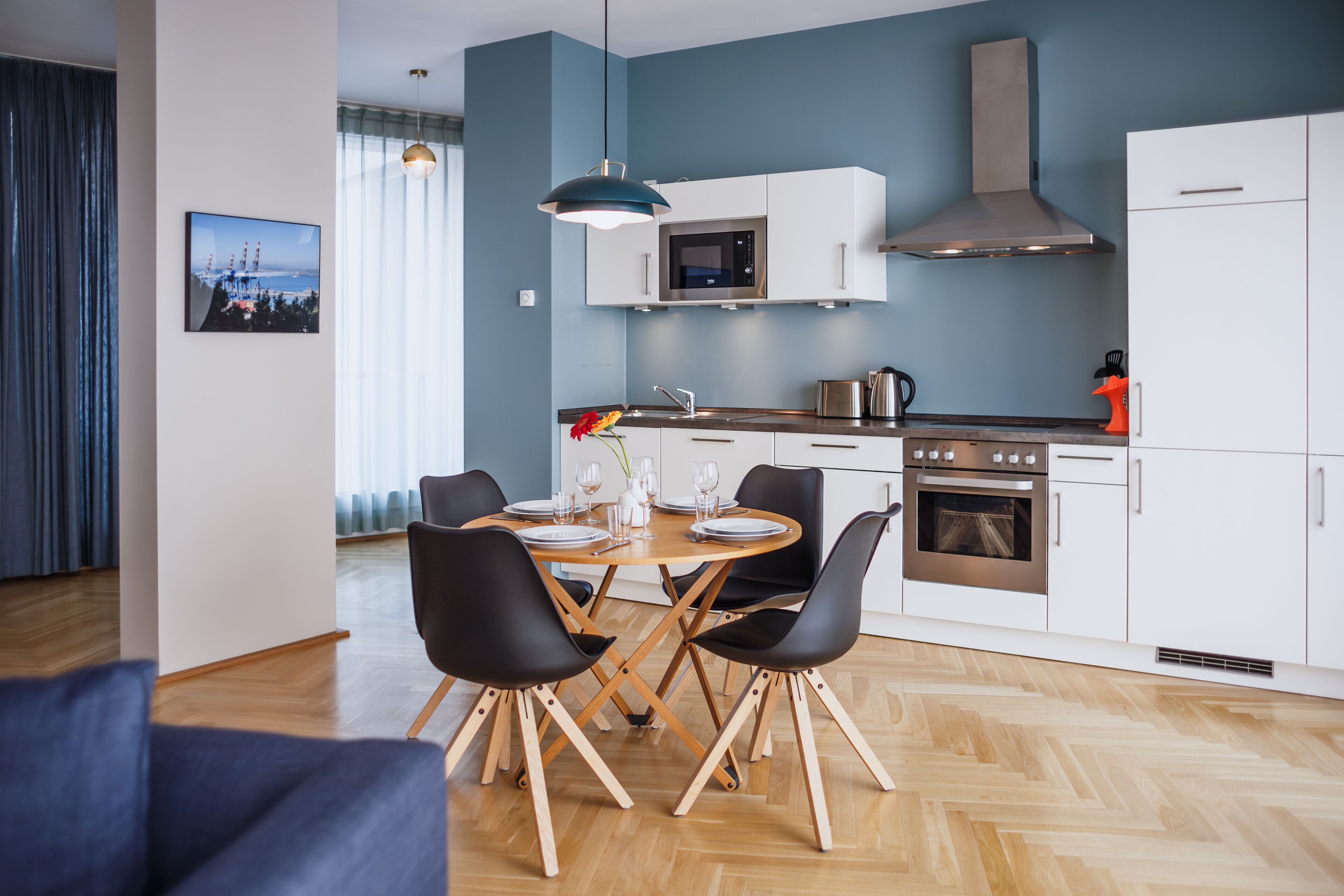 Una cocina moderna con armarios blancos, una campana extractora de acero inoxidable y un comedor con mesa de madera y sillas negras.