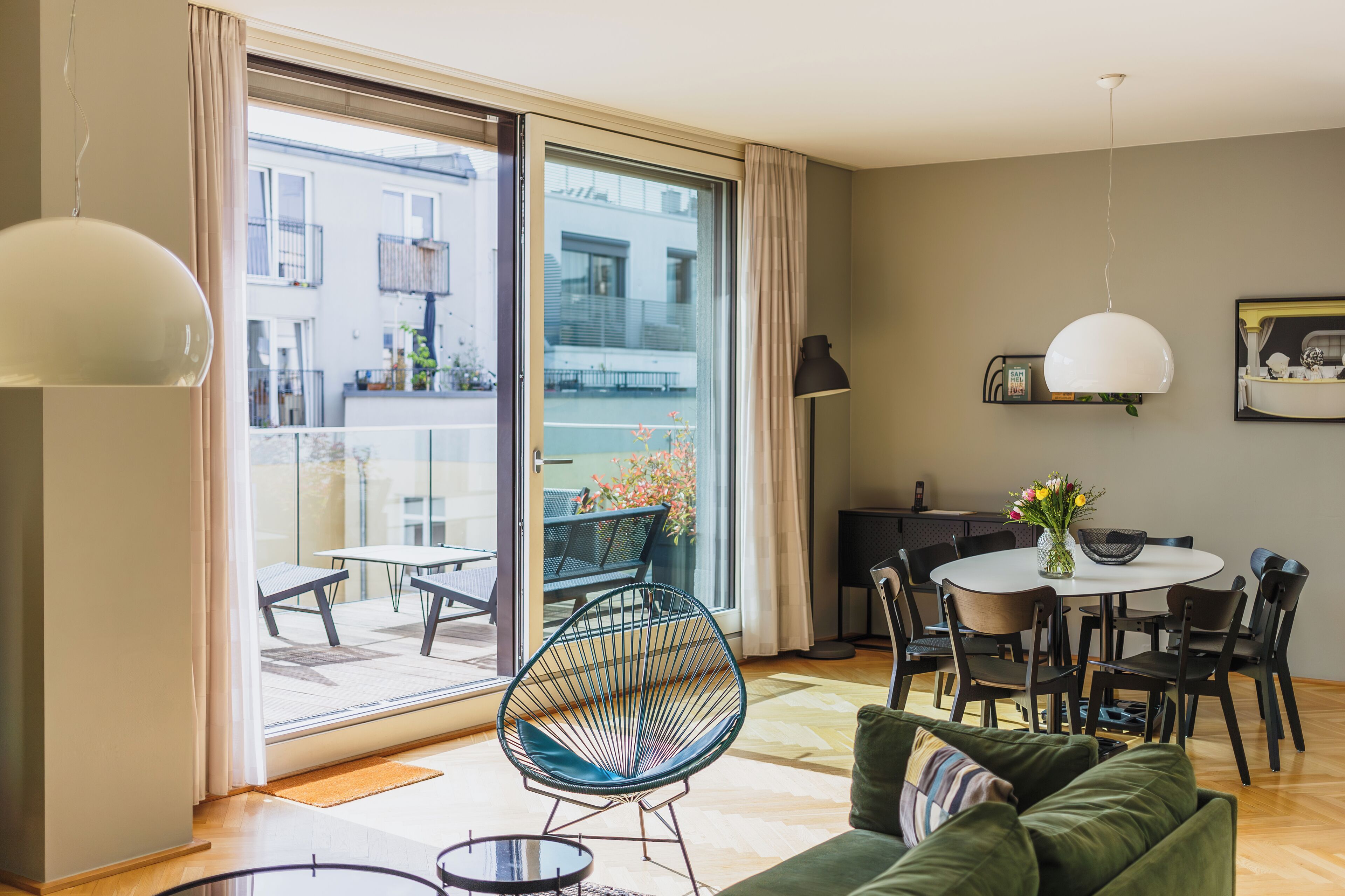 En moderne stue med en grøn sofa, et spisebord med stole, et rundt sofabord og et stort vindue med udsigt ud