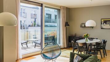 En moderne stue med en grøn sofa, et spisebord med stole, et rundt sofabord og et stort vindue med udsigt ud