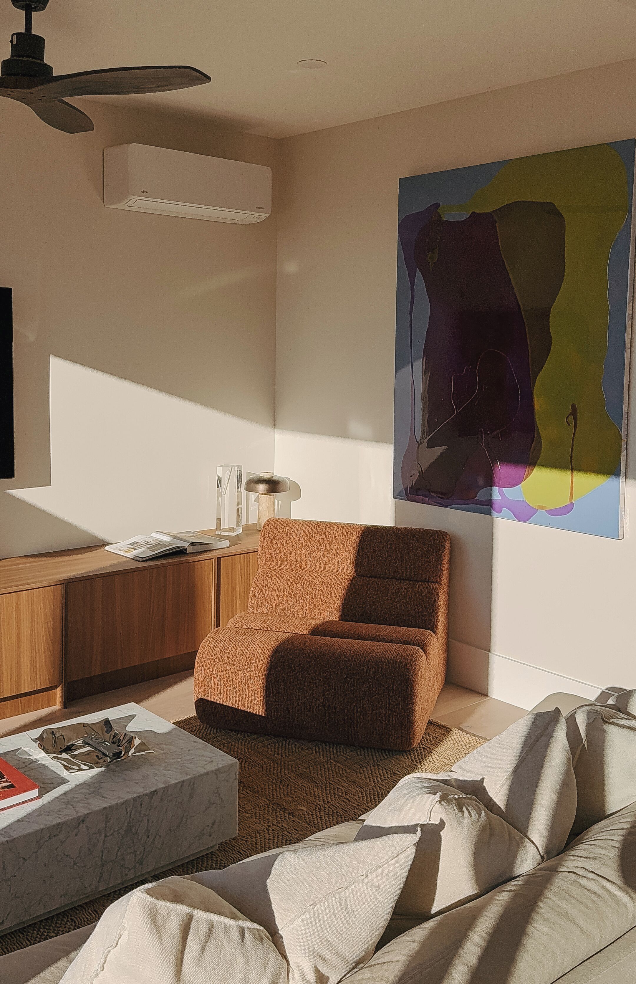 Una sala de estar moderna con un sofá, una mesa de centro, una lámpara, un televisor y un cuadro abstracto grande en la pared.