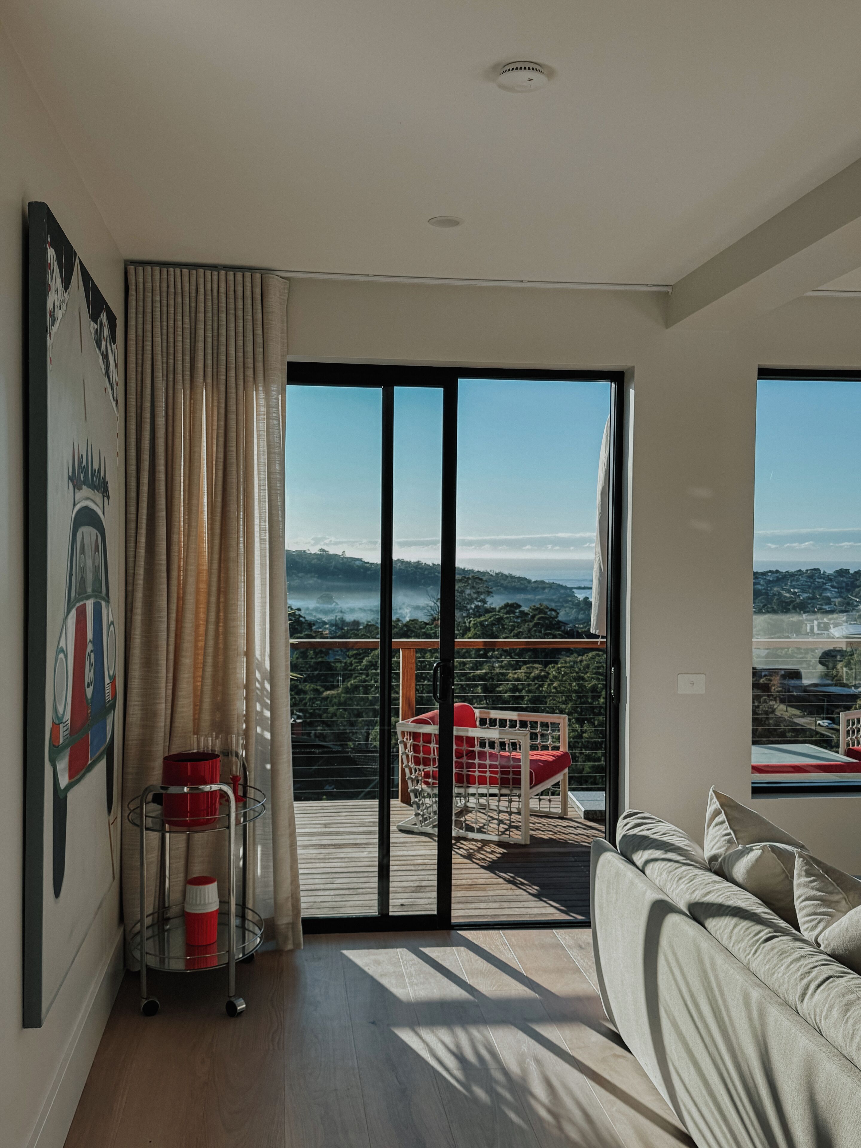 A modern living room with a large sliding glass door leading to a balcony with a view of a coastal landscape.