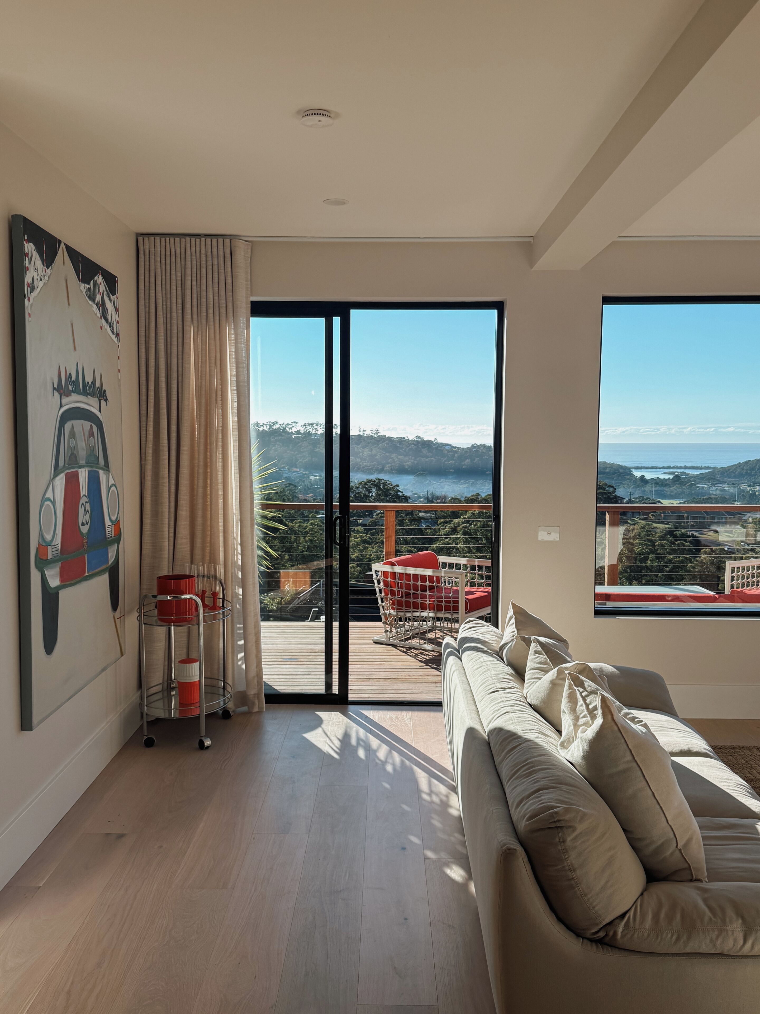 A spacious room with a large sliding glass door leading to an outdoor deck, a beige sofa, and a painting on the wall.