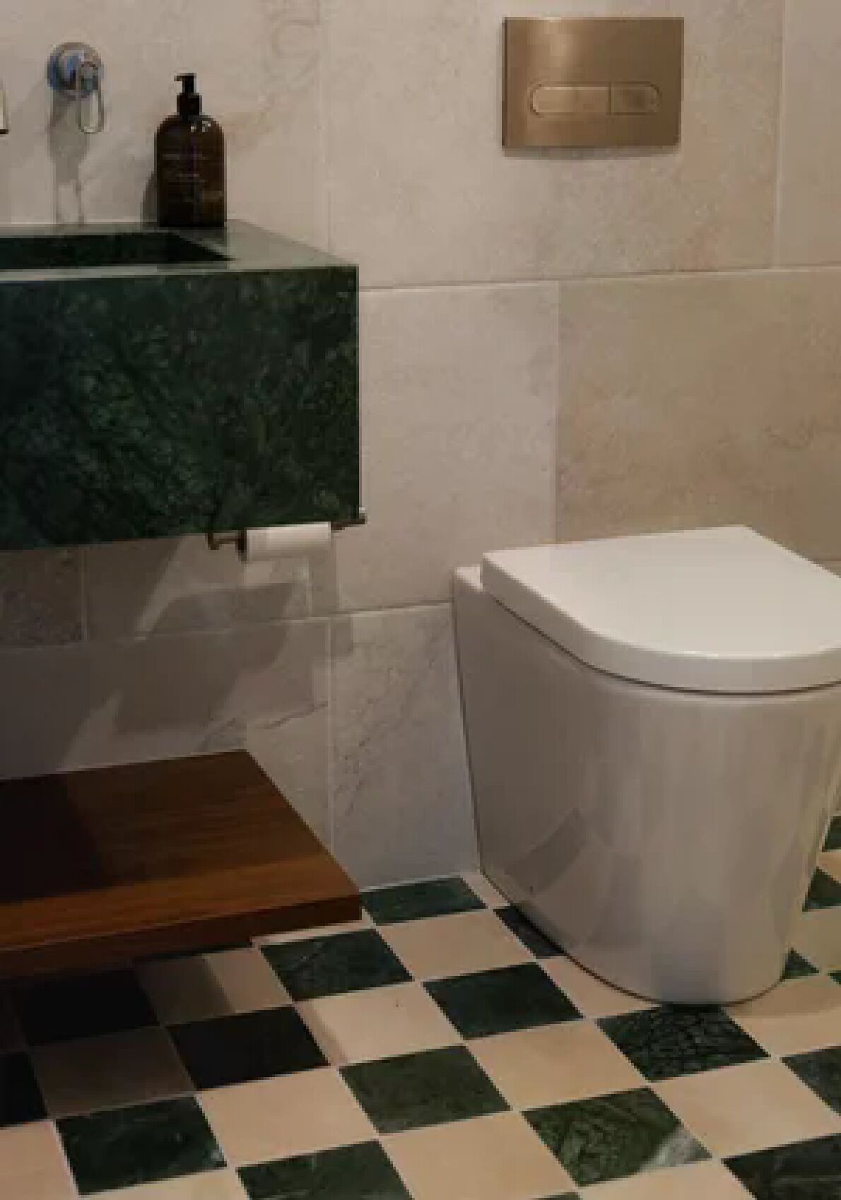 A bathroom with a checkered floor, a white toilet, a green marble sink, and a soap dispenser.