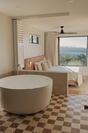 A modern bedroom with a large bathtub, a bed with a view, and a ceiling fan. - Hillcrest Merimbula (Merimbula)