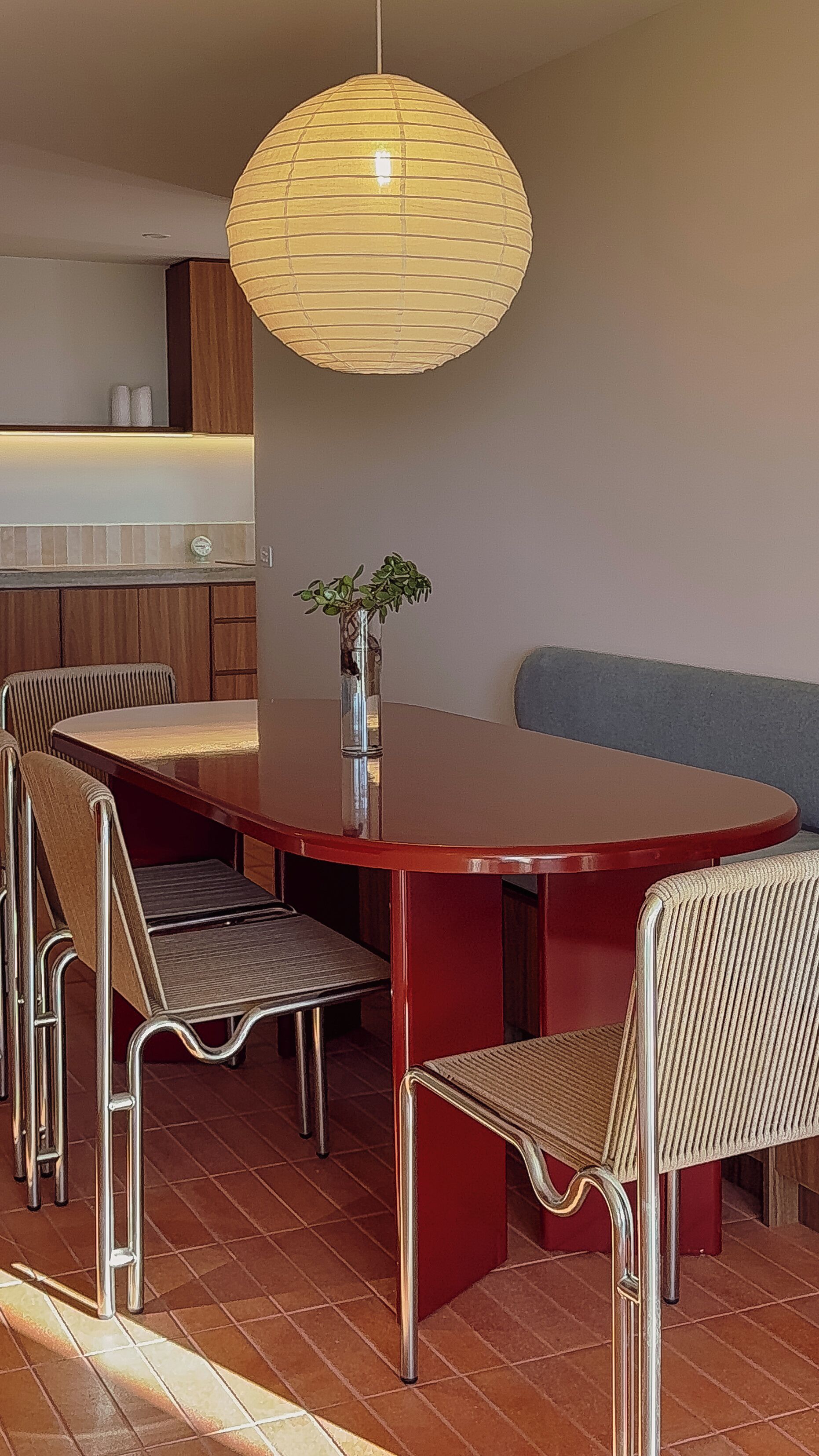 Un comedor con una mesa redonda, seis sillas, una lámpara colgante y una planta pequeña sobre la mesa.