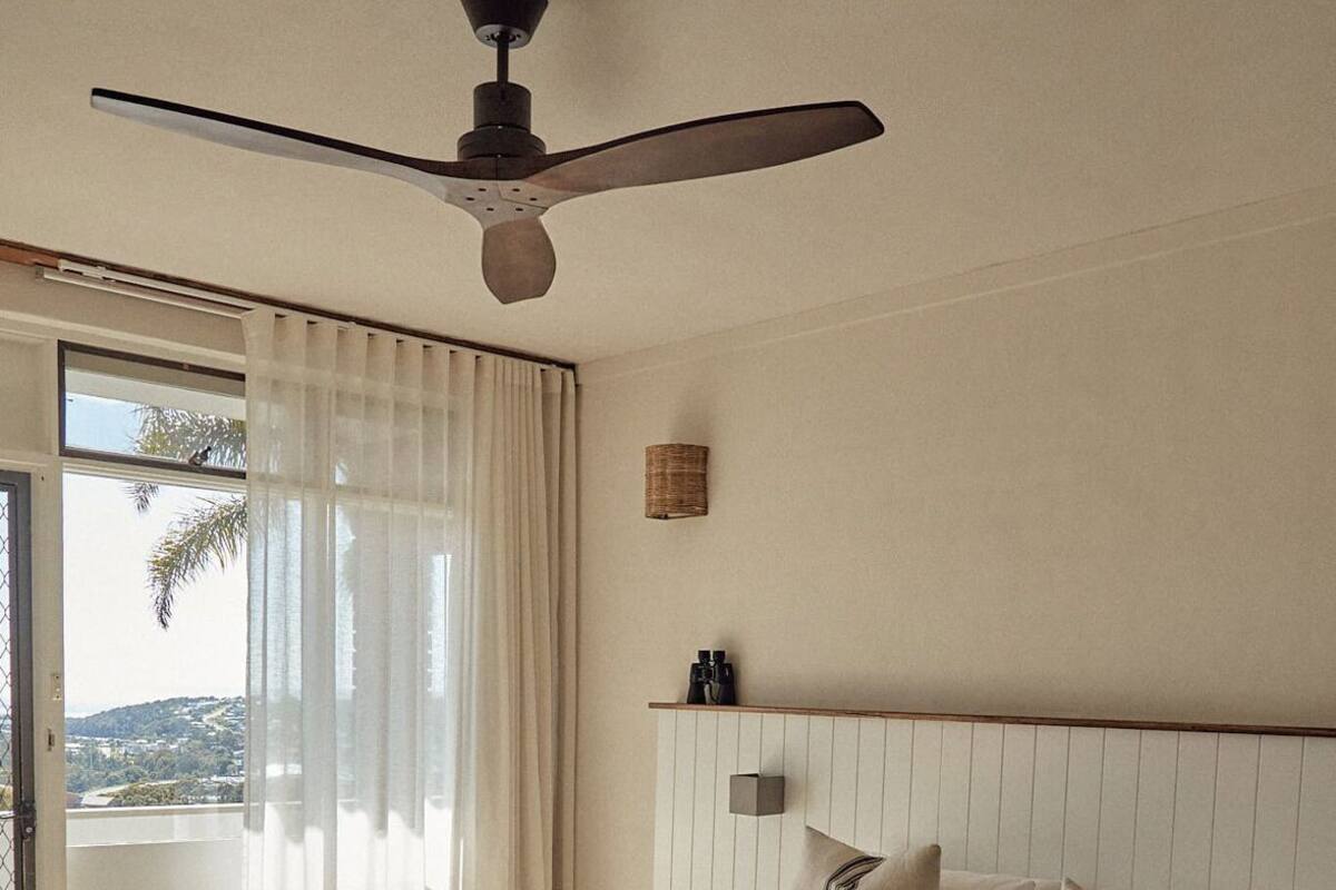 Une chambre à coucher avec un lit, un ventilateur de plafond, une fenêtre avec des rideaux et une vue sur l’extérieur.