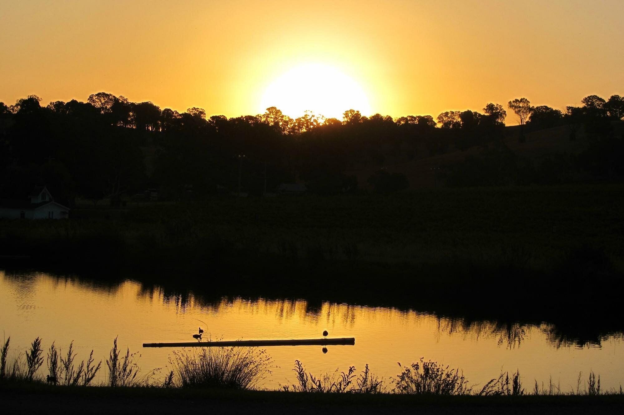A sunset over a calm lake with a dock and a house in the background.