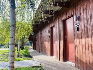 A row of wooden doors with a sign above each, a covered walkway, and a tree in the foreground.