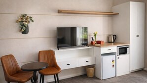 A compact kitchenette with a TV, microwave, and small fridge, a dining area with two chairs, and a wooden shelf above the TV. - De'Vine Escape (Dixons Creek)