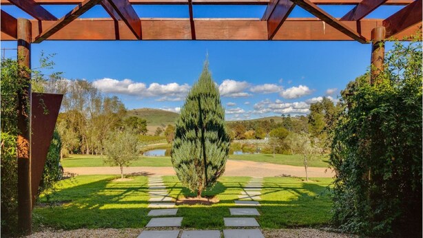 A gazebo with a clear view of a well-maintained garden, a central tree, and a distant body of water. - De'Vine Escape (Dixons Creek)