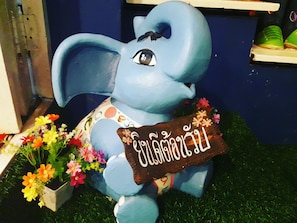Une statue d’éléphant bleue, avec une pancarte, entourée de fleurs.
