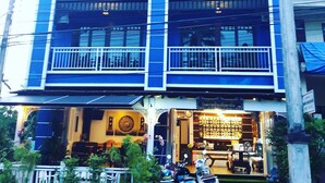 A multi-story building with balconies, a ground-level shop, and potted plants.