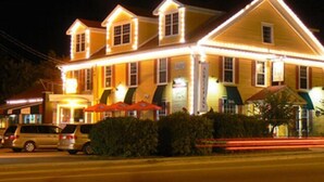A two-story building with a yellow facade and multiple windows, featuring a well-lit entrance and a covered outdoor seating area. - L'Auberge Gabrièle Inn (Shediac)