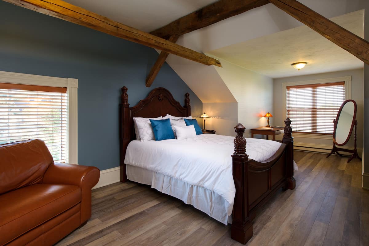 A bedroom with a wooden bed, a leather sofa, and a sloped ceiling with exposed beams.