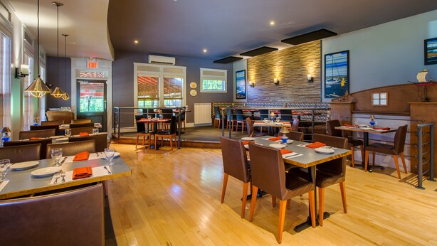 A modern restaurant with wooden flooring, multiple dining tables, and contemporary lighting fixtures. - L'Auberge Gabrièle Inn (Shediac)