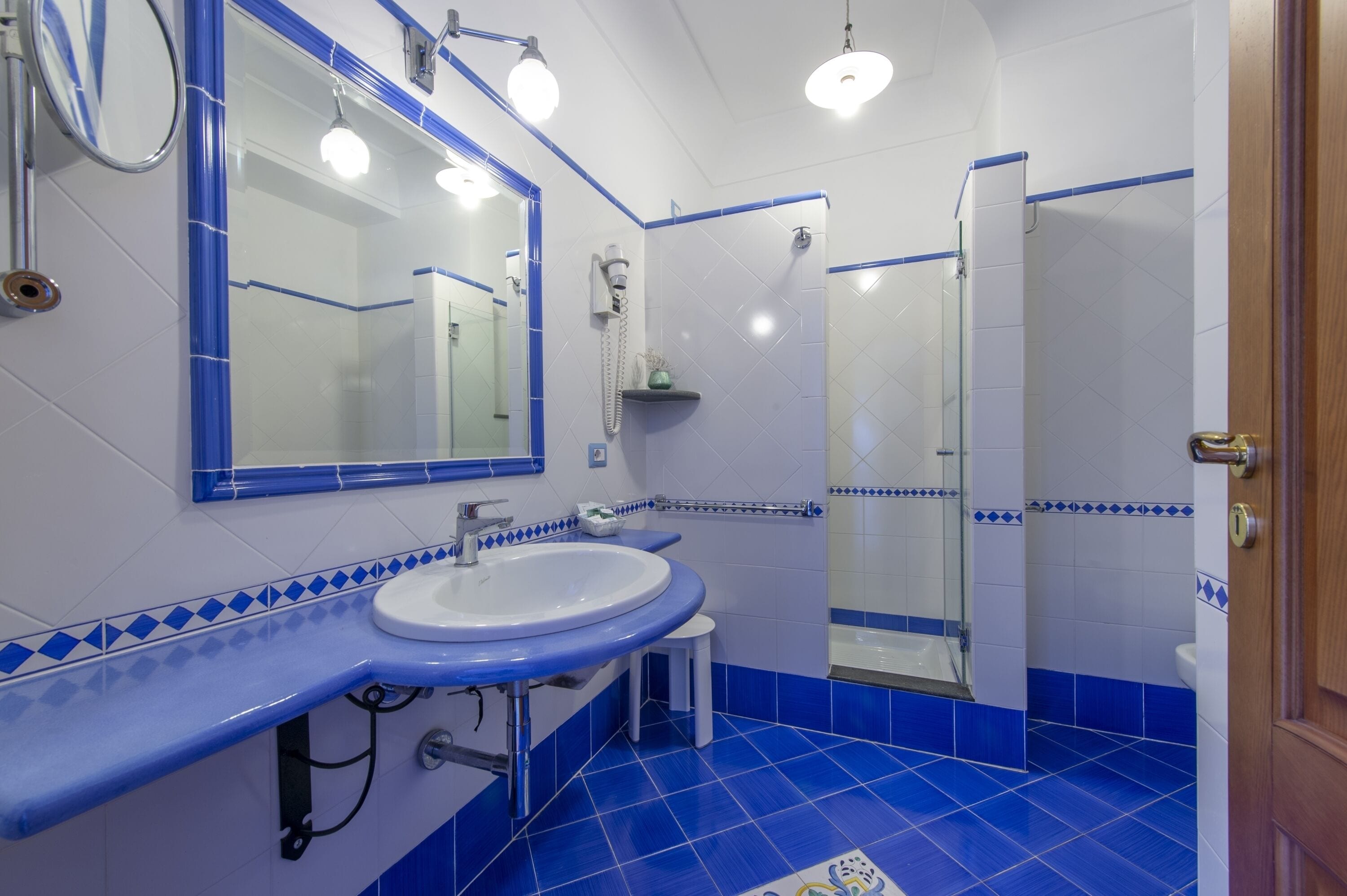 A bathroom with a white sink, blue-tiled floor, and a glass shower enclosure.