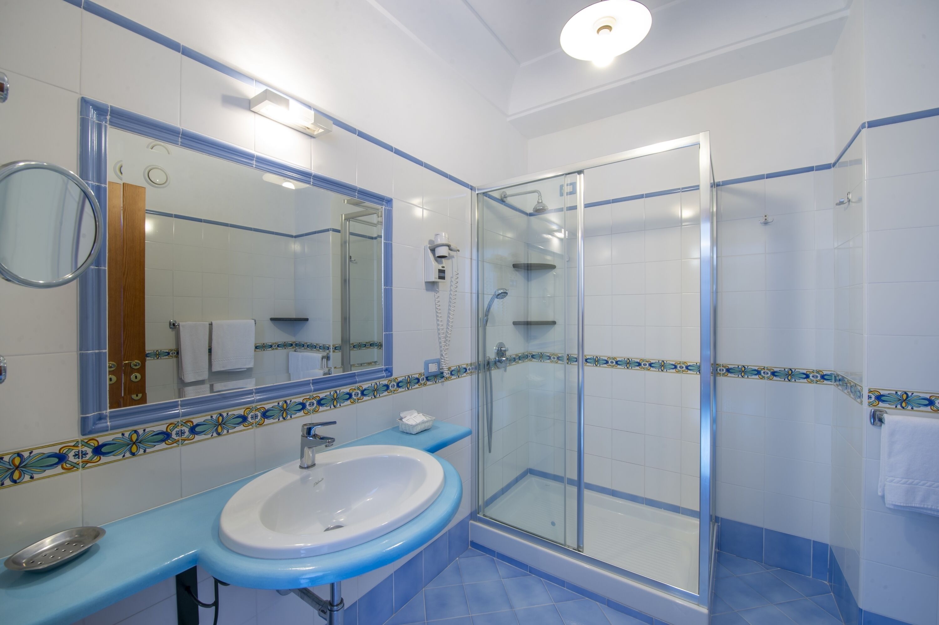 A bathroom with a glass-enclosed shower, a sink with a blue countertop, and a mirror with a wooden door reflection.