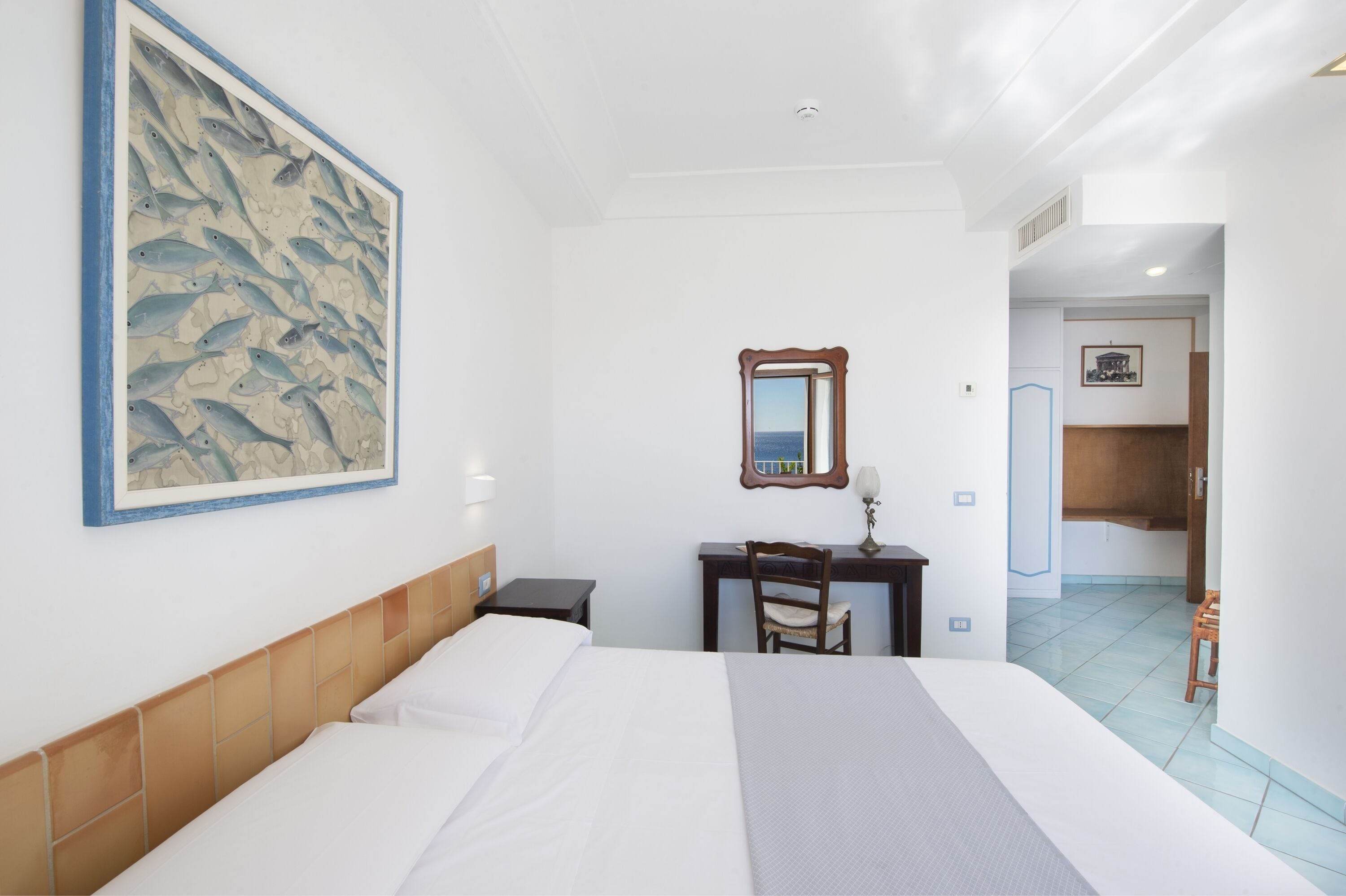Ein Hotelzimmer mit einem Bett, einem Schreibtisch, einem Sessel und einem Spiegel, sowie einem großen Wandbild mit Fischen.