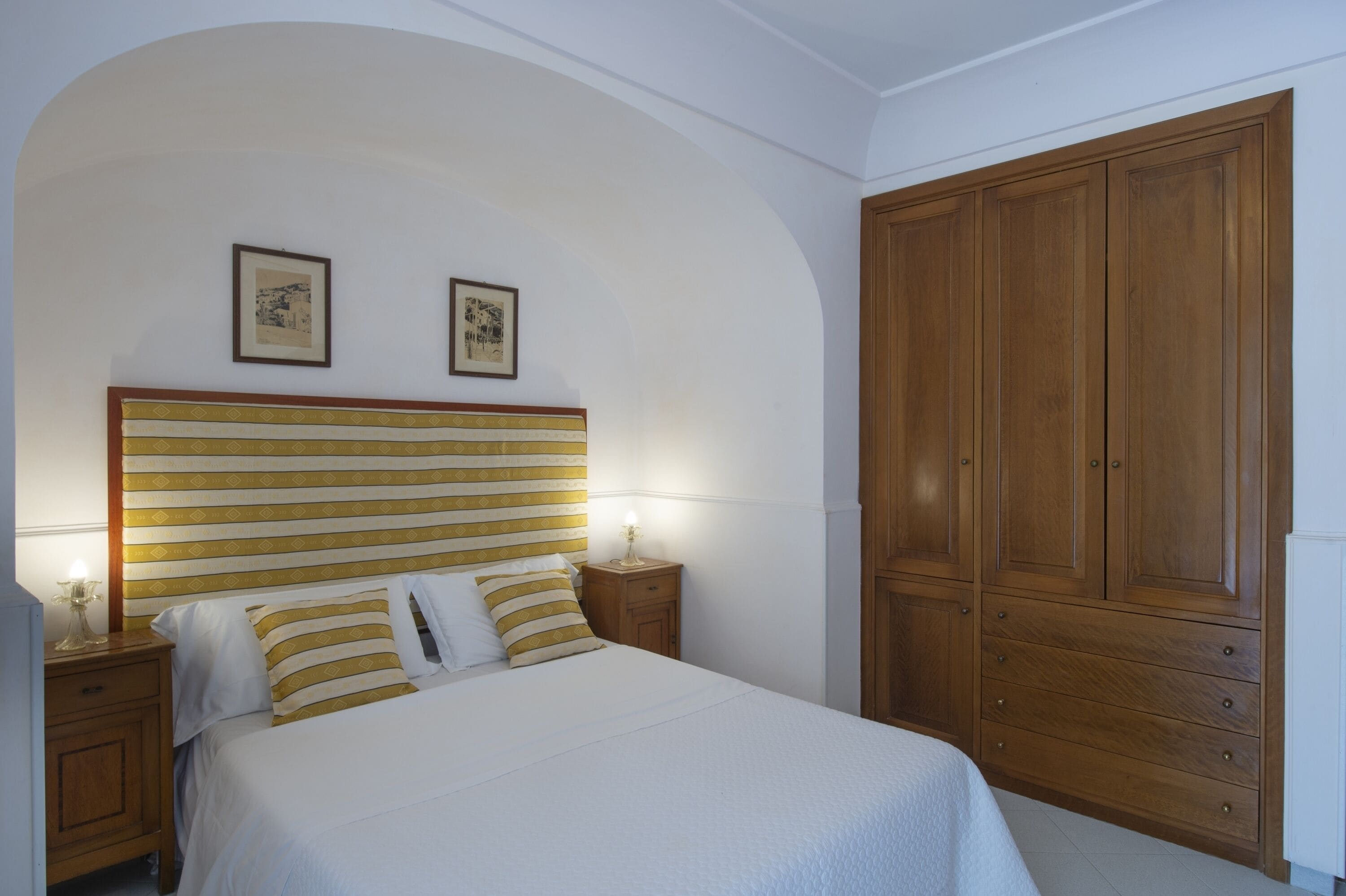 A bedroom with a large bed, wooden wardrobe, and two framed pictures on the wall.