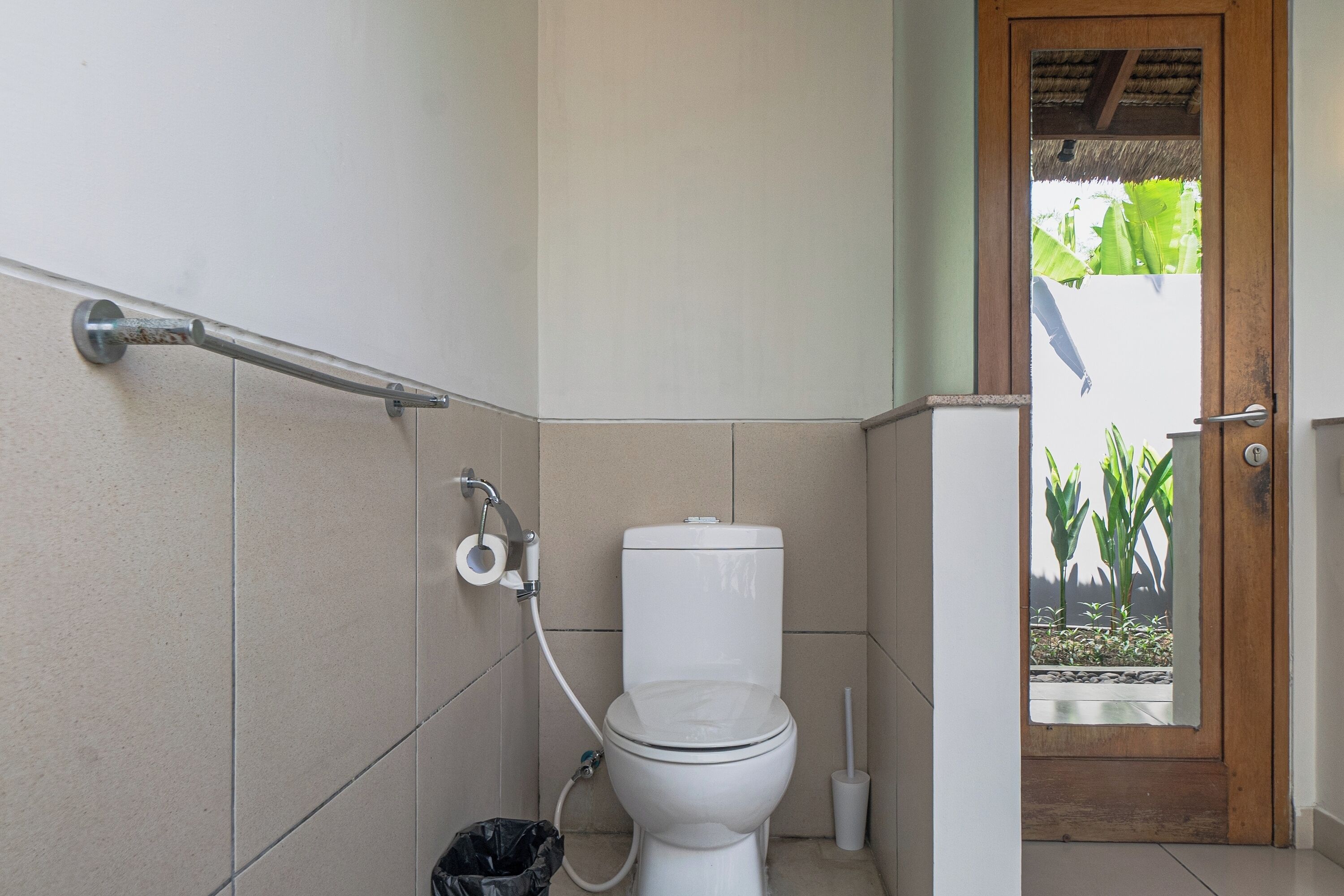 Bagno con il water, una maniglia e vista su un giardino attraverso una porta.