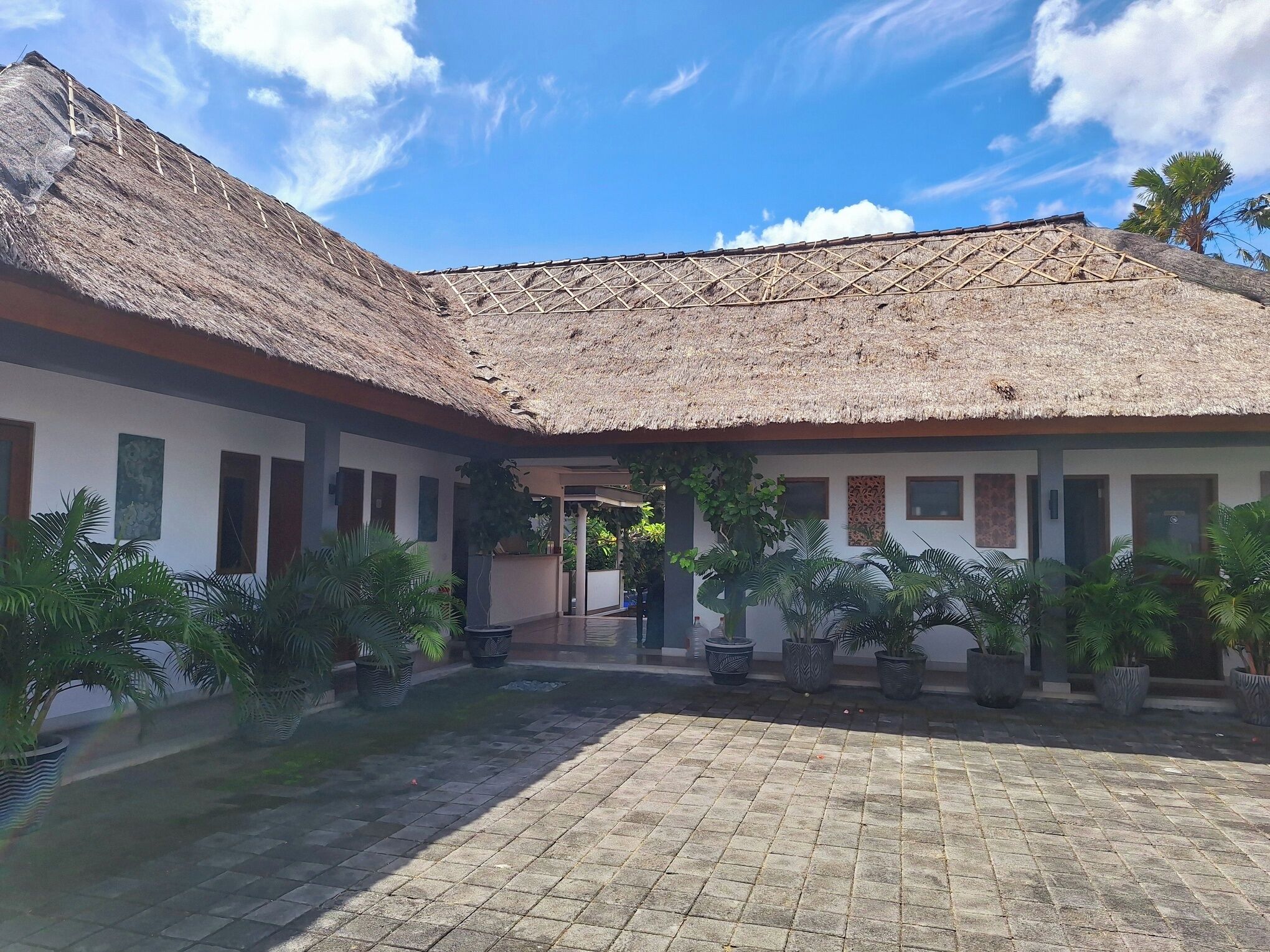 A courtyard with a thatched roof, potted plants, and a paved walkway.