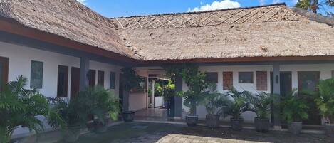 A courtyard with a thatched roof, potted plants, and a paved walkway.
