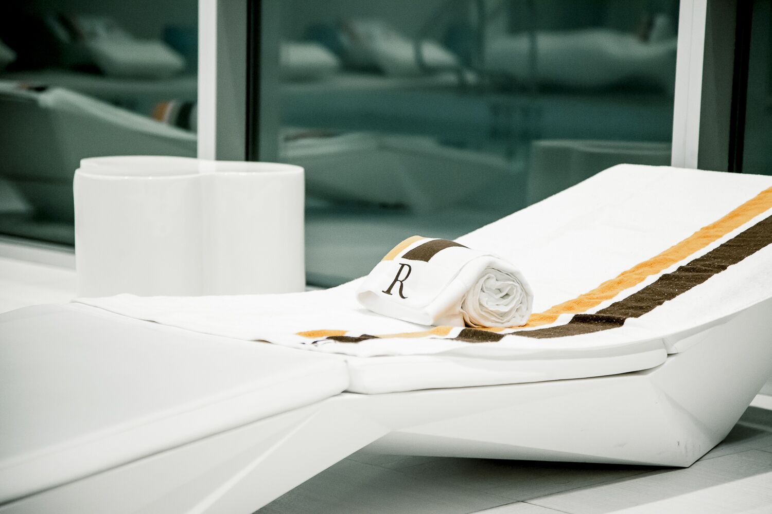 A white sun lounger with a towel and a towel with a letter 'R' on it.