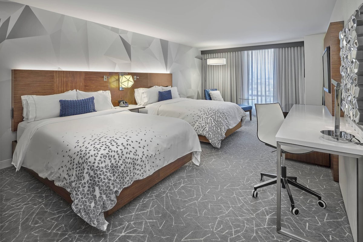 A hotel room with two beds, a desk, and a chair.
