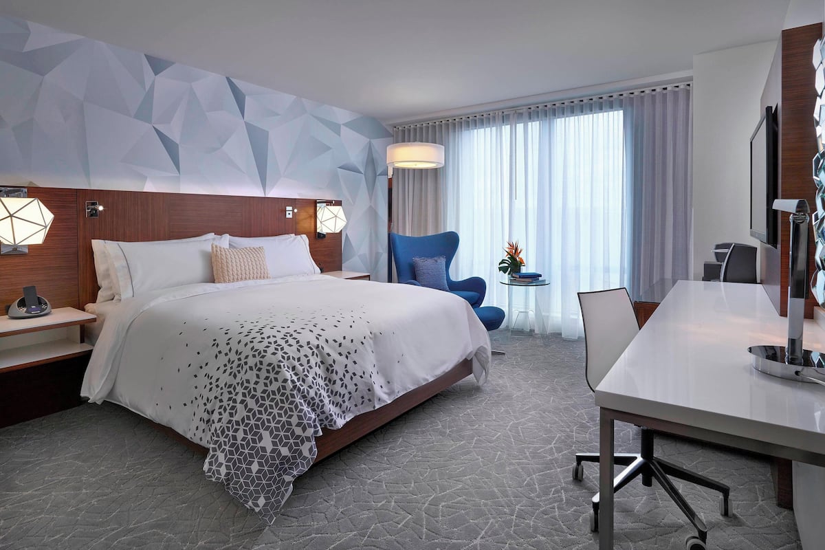 A hotel room with a large bed, a desk, a chair, and a TV.