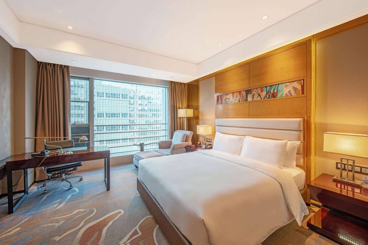 Ein Hotelzimmer mit einem großen Bett, einem Schreibtisch, einem Sessel und einem Fenster mit Vorhängen.