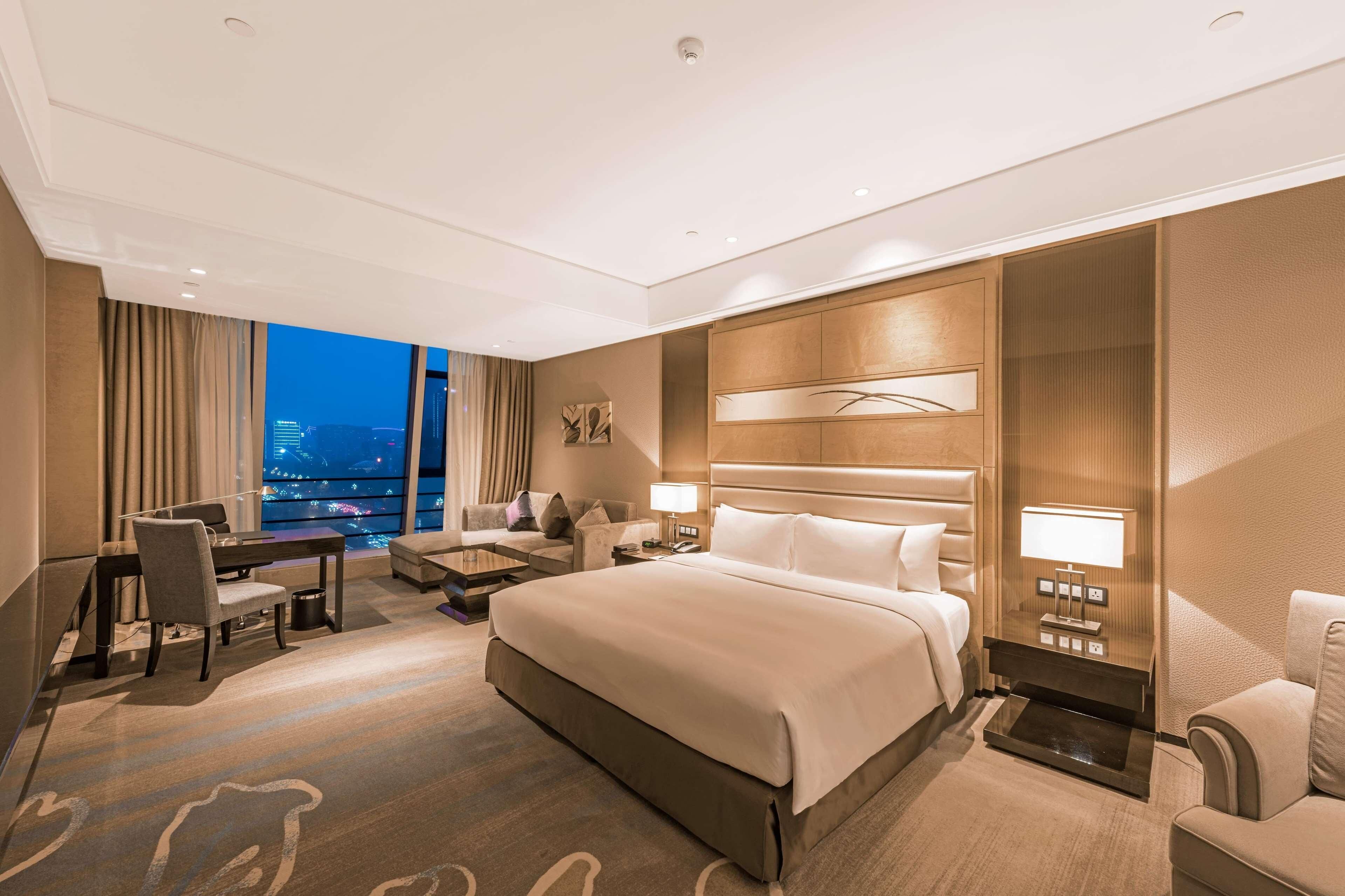 Una habitación de hotel moderna con una cama grande, un escritorio, un sofá y vistas a la ciudad.