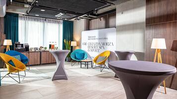 A modern hotel lobby with a reception desk, seating area, and a large informational board.