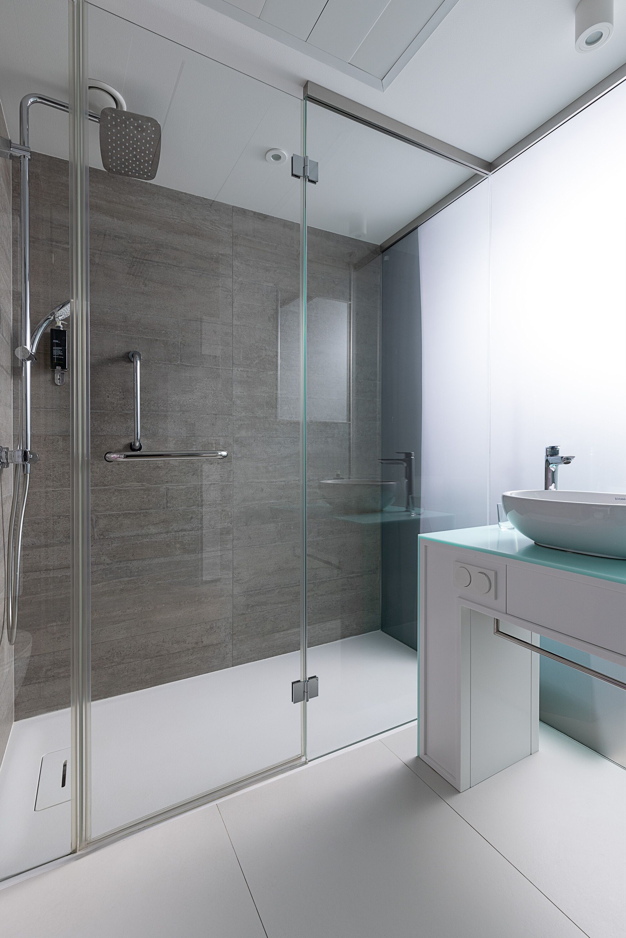 Ein modernes Badezimmer mit Duschabtrennung aus Glas, integriertem Waschbecken und Spiegel.