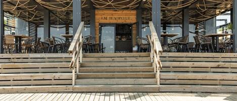 A wooden deck with outdoor seating, a wooden staircase, and a sign reading "GM BEACH CLUB".