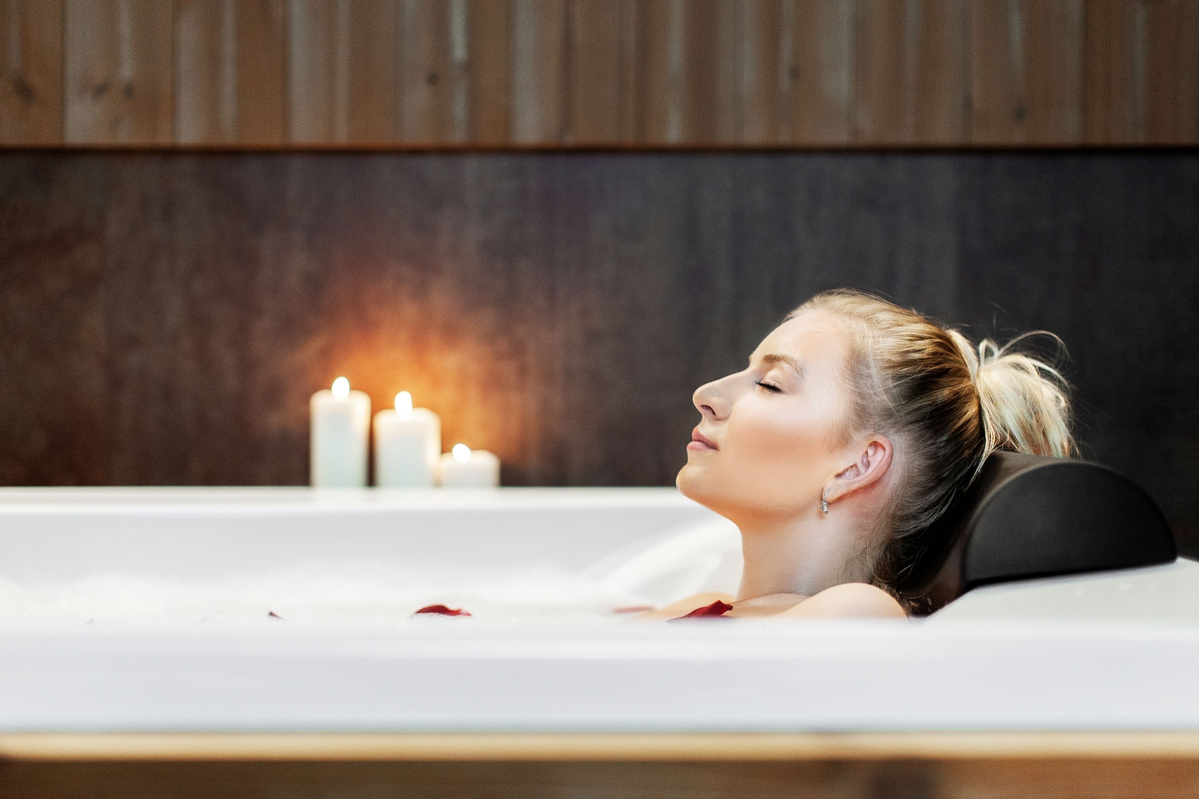 A person relaxing in a bathtub with candles in the background.