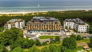 A modern building with multiple floors, surrounded by lush greenery and a view of the sea.