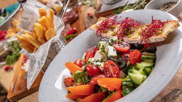 A plate of fresh salad with tomatoes, cucumbers, and cheese, accompanied by a side of fries and slices of bread with sprouts.
