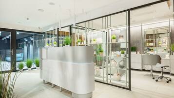 A modern reception area with a white reception desk, glass display shelves, and potted plants.