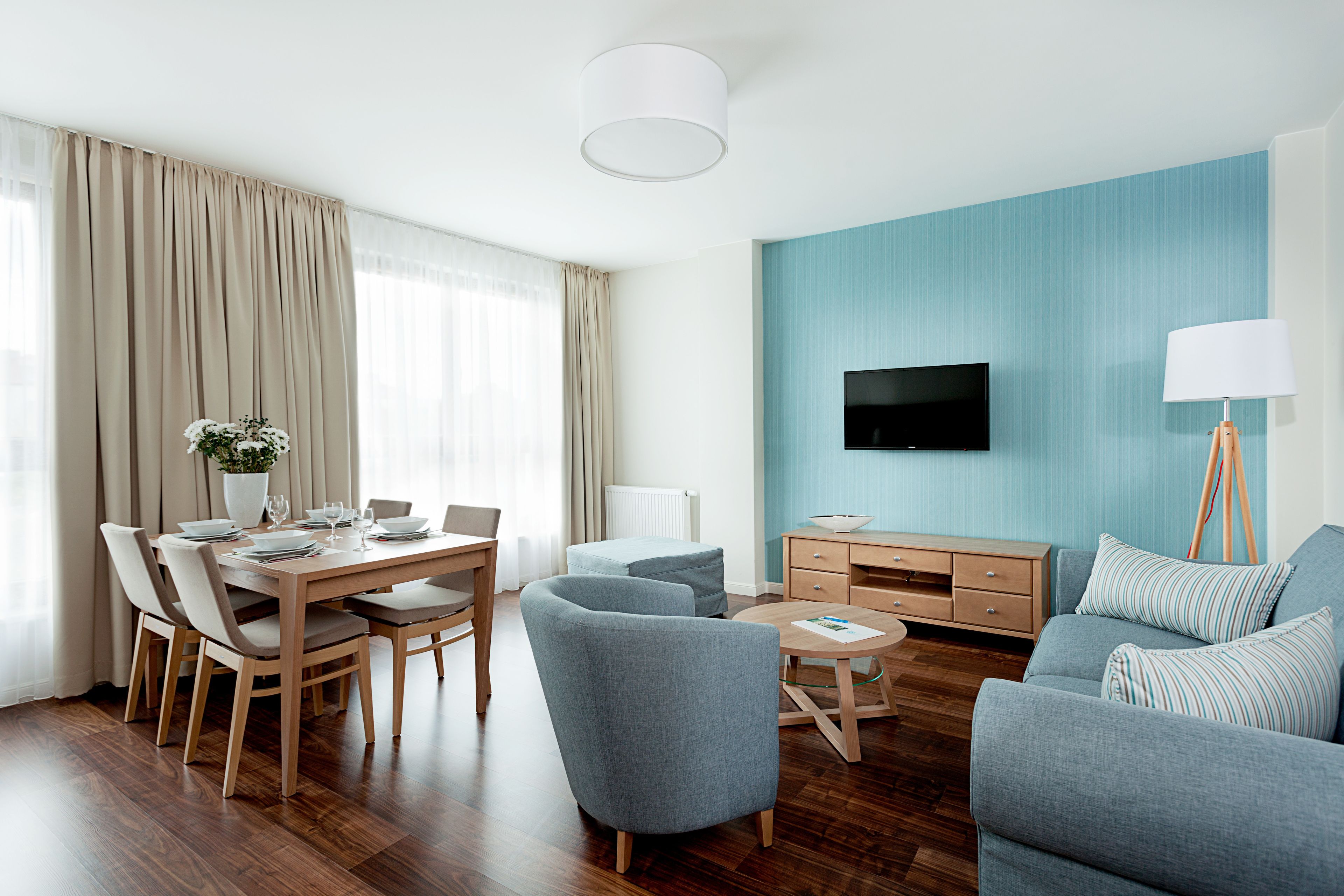 Una sala de estar moderna con comedor, un conjunto de sofás, un televisor montado en la pared y una lámpara.