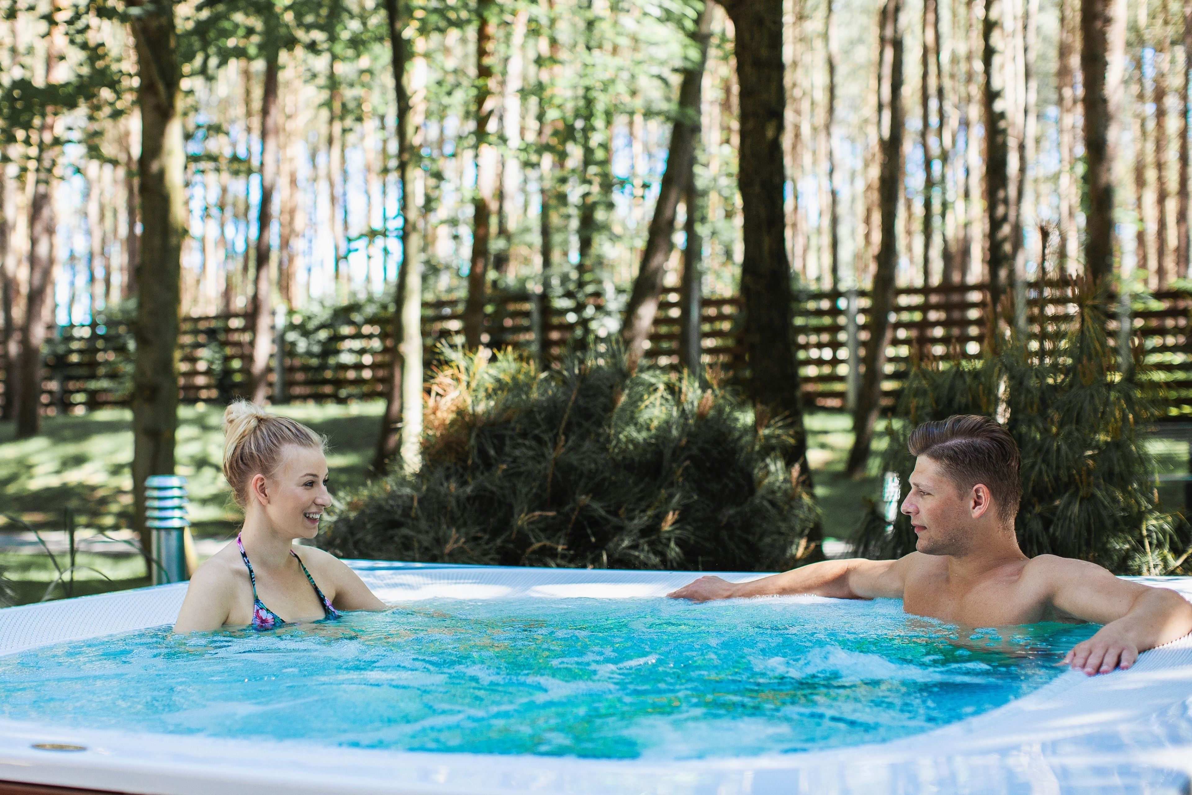 A hot tub in a wooded area with a wooden fence and trees in the background.