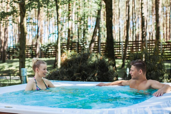 Un jacuzzi en un área boscosa con una valla de madera y árboles al fondo.