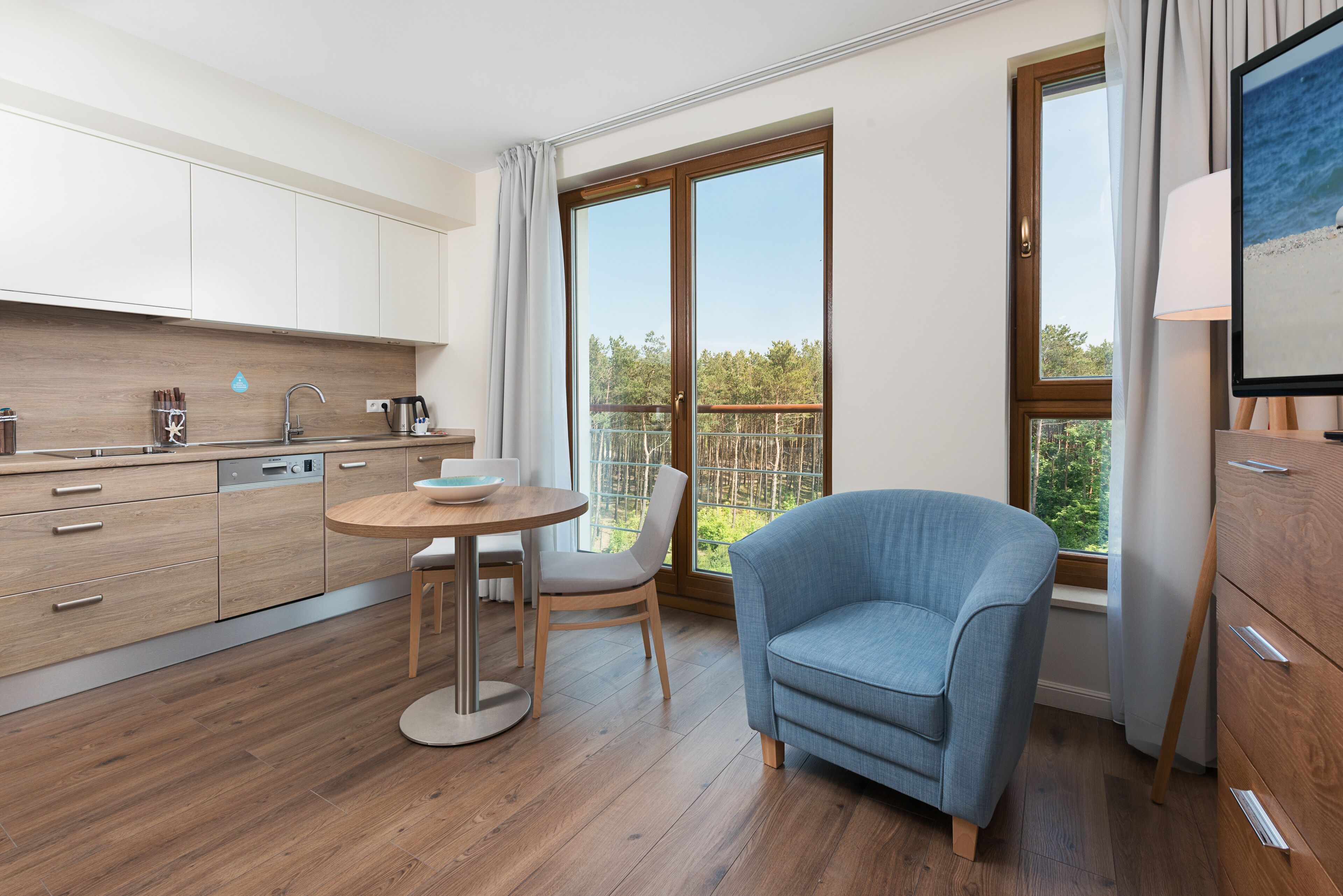 A modern kitchen with wooden cabinets, a round dining table, and a blue armchair.