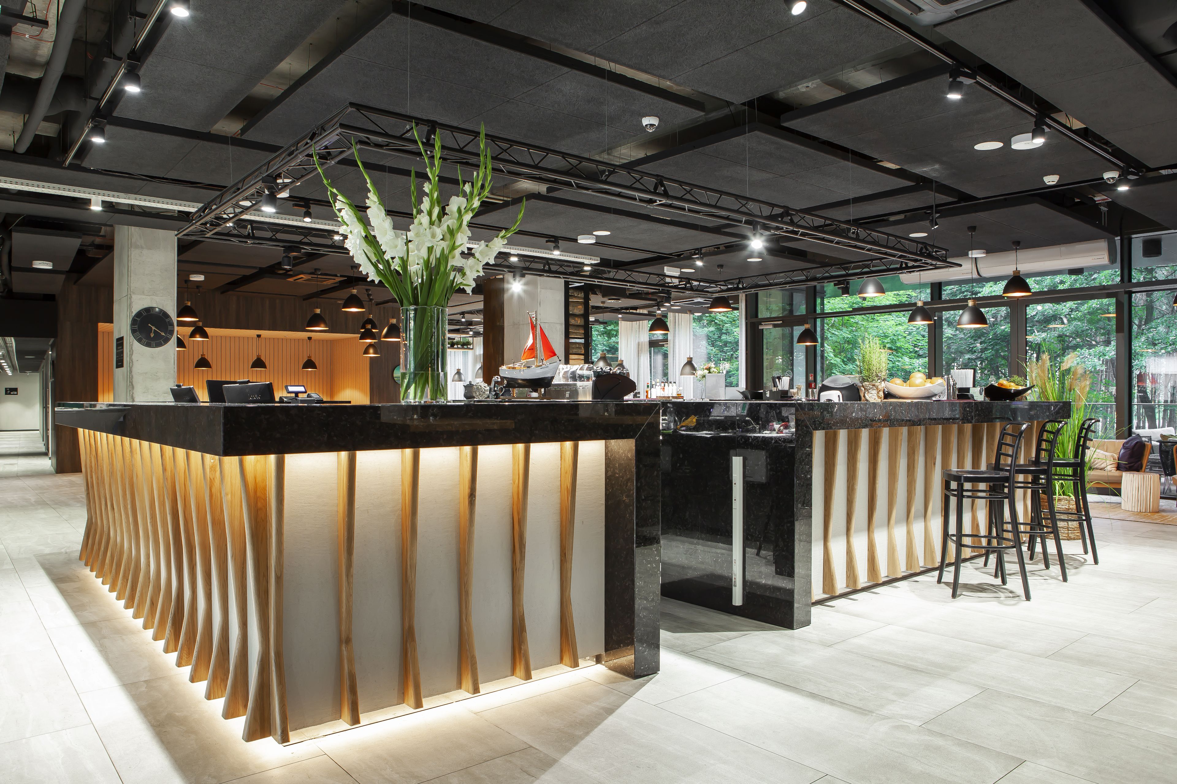 Un área de bar moderna con un diseño de madera original, un jarrón grande con flores y vistas al exterior con vegetación.