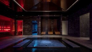 A modern spa with a central water feature, stone walls, and red ambient lighting.