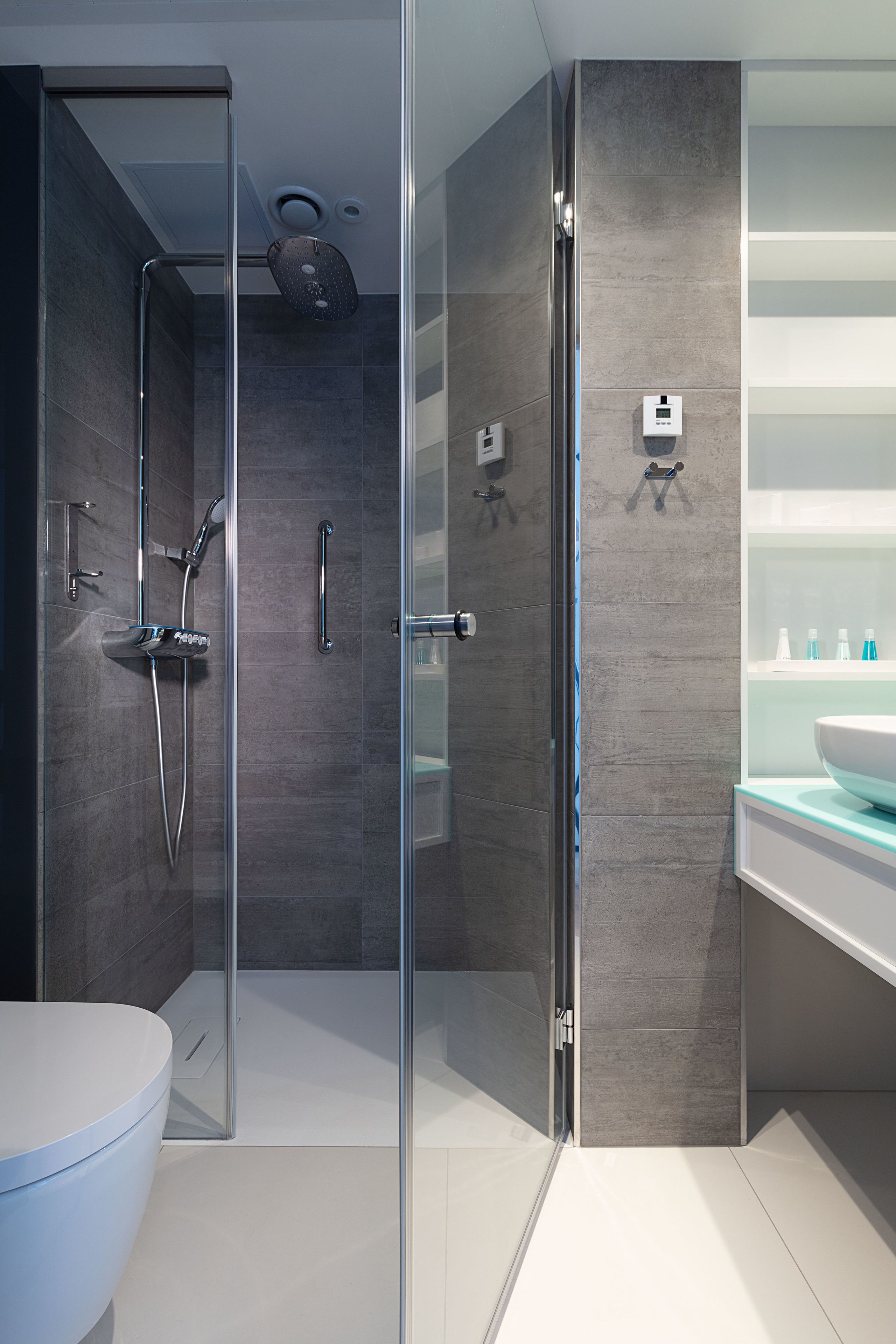 A modern bathroom with a glass shower enclosure, a white toilet, and a vanity with a large mirror and a sink.