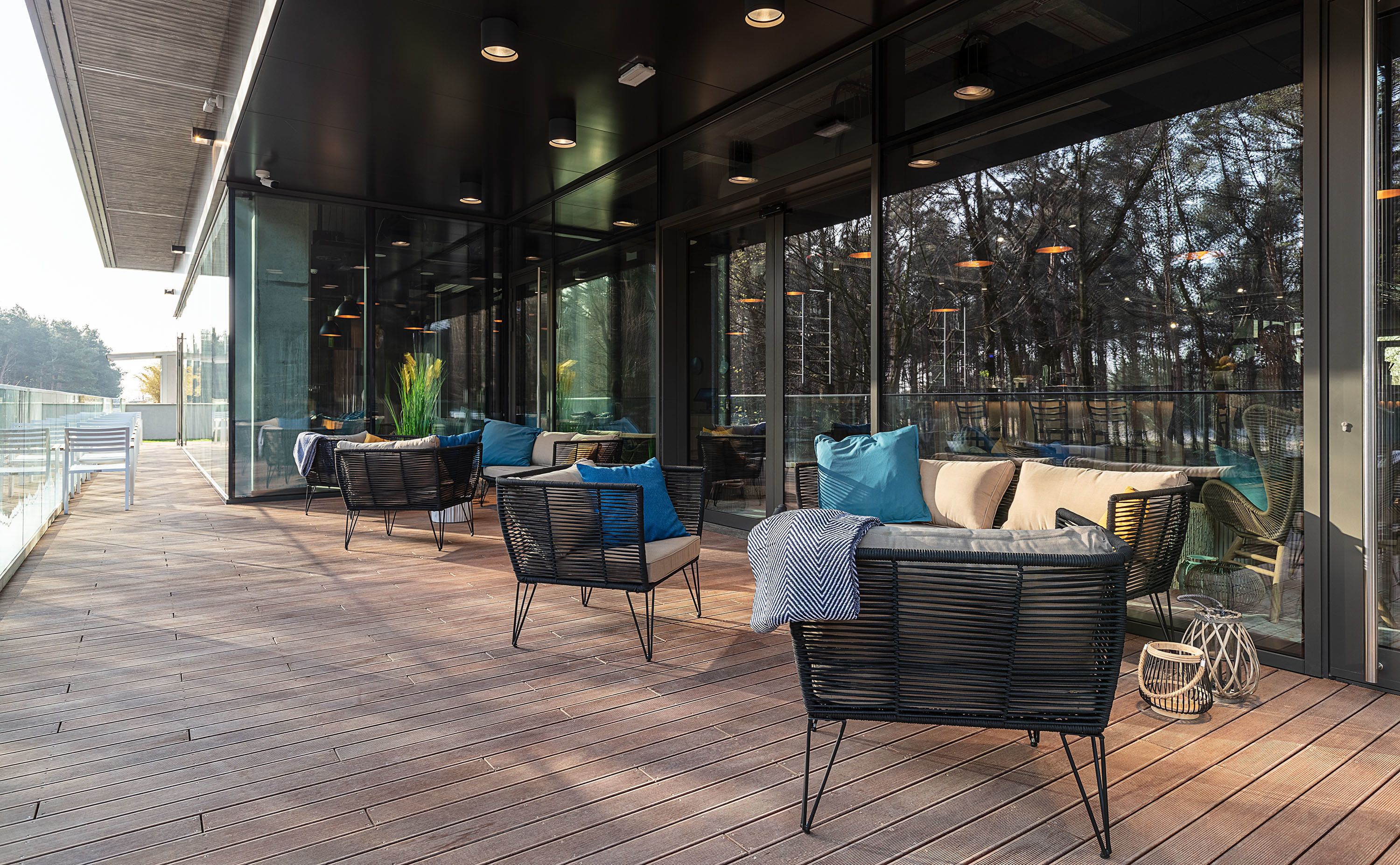 A modern outdoor seating area with wicker furniture and large windows offering views of trees.