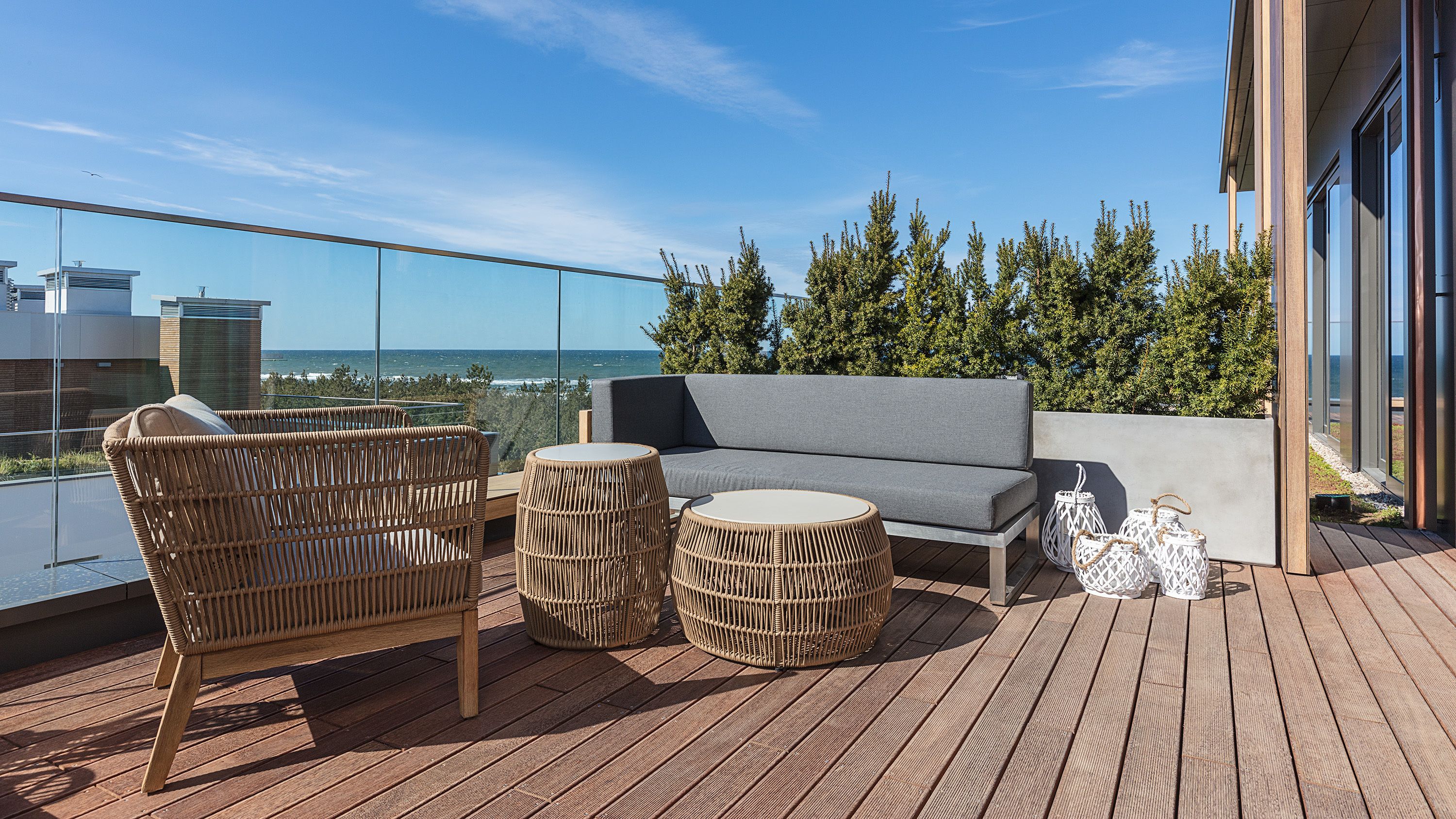 A balcony with wicker furniture, a grey sofa, and round tables.