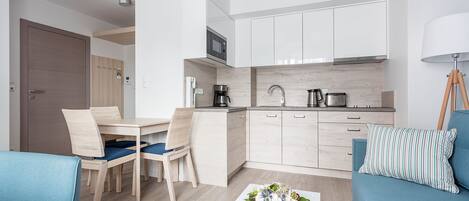 A modern kitchen with white cabinets, a microwave, and a coffee maker. There is a dining area with a table and chairs, and a blue sofa with a striped pillow.